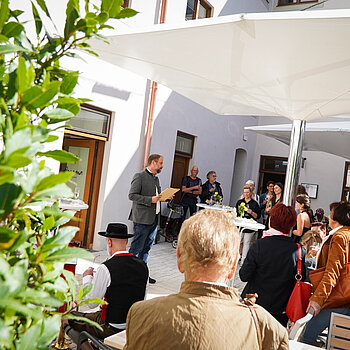 Auf dem Foto ist die Eröffnungsrede von Oberbürgermeister Tobias Eschenbacher vor dem dASAMa Dialograum zu sehen. Die Aufnahme wurde seitlich gemacht, um die Atmosphäre während der Rede einzufangen. Die Sonne scheint, und der Innenhof des dASAMa ist gut gefüllt. Die Stimmung wirkt angenehm und positiv.