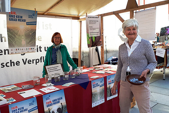 eine Frau vor und eine hinter dem Stand laden zum Abstimmen mit Puzzleteilen in verschieden Gläsern ein