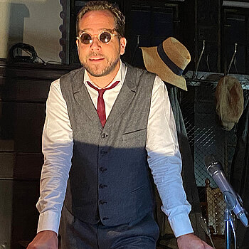 Ein Mann mit Sonnenbrille und rotem Schlips vor einer Garderobe.