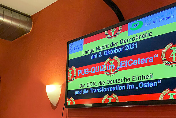 Bildschirm mit DDR-Emblem auf Schwarz-Rot-Gold und "Pub-Quiz im EtCetera"