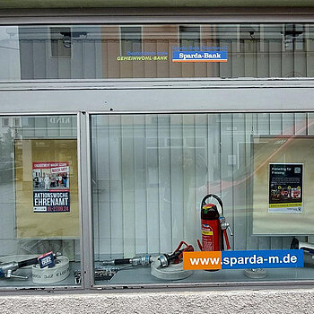 in einem Schaufenster sind Feuerlöscher und Schläuche ausgestellt sowie Infoplakate 