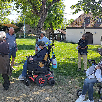 Kleine Stadtführung nach dem Mittagessen. Foto: Stadt Freising eine Gruppe Menschen teils mit Rollstuhl und Rolator in einer Grünanlage