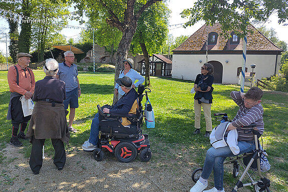 Kleine Stadtführung nach dem Mittagessen. Foto: Stadt Freising eine Gruppe Menschen teils mit Rollstuhl und Rolator in einer Grünanlage