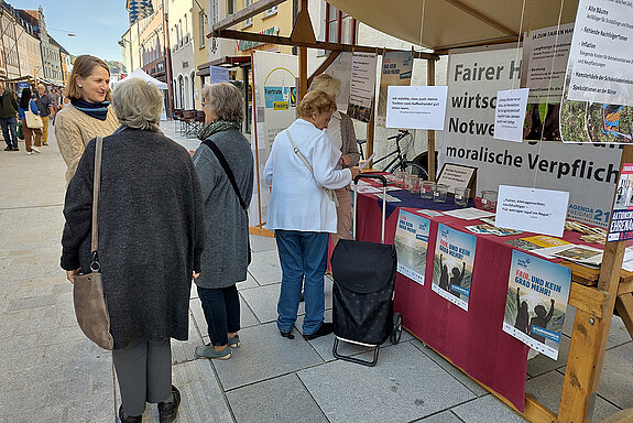 Eine Frau spricht mit zwei älteren Damen während zwei weitere Frauen direkt am Stand stehen und sich unterhalten.