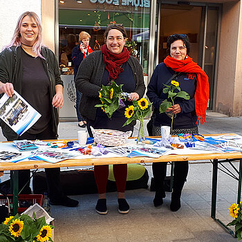 drei Frauen hinter einem Infotisch mit verschiedenen Materialien und geschmückt mit Sonnenblumen