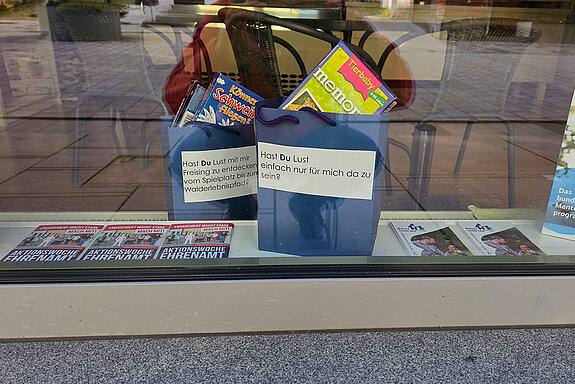 zwei blaue Taschen mit Beschriftung und Spielmaterial im Fenster