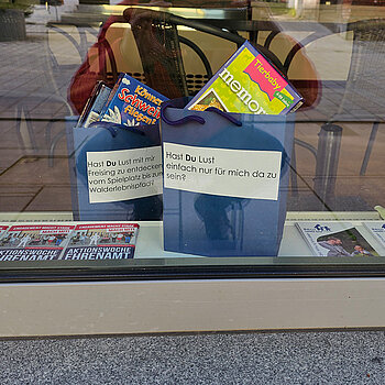 zwei blaue Taschen mit Beschriftung und Spielmaterial im Fenster